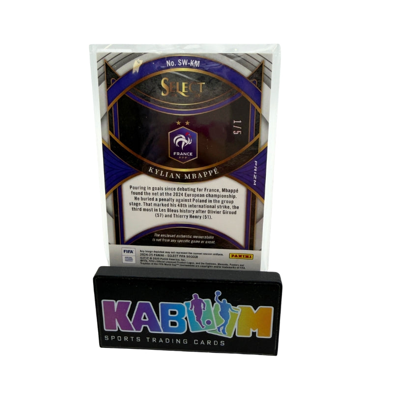 A collectible sports trading card displayed in a clear protective case on a black acrylic stand. The card is for Kylian Mappé and features Panini branding, with the stand displaying 'KABOOM SPORTS TRADING CARDS'.